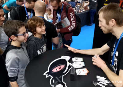 un maitre du jeu explique les règles à des visiteurs du stand